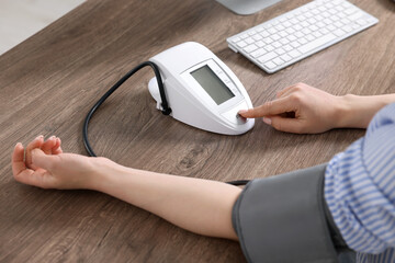 Fototapeta premium Woman measuring blood pressure at wooden table, closeup
