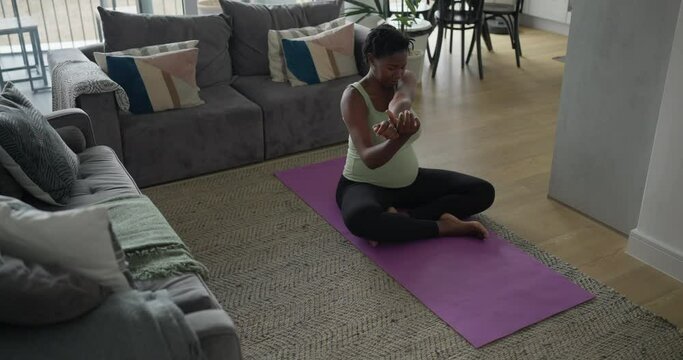 Pregnant woman stretching arms on exercise mat in living room