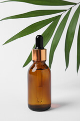 Bottle with cosmetic oil and green leaf on white background