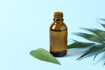 Bottle of cosmetic oil and leaves on light blue background, closeup