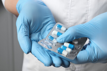 Doctor taking pill out from blister pack on grey background, closeup