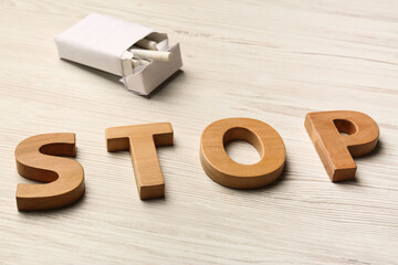 Pack with cigarettes and word Stop made of letters on white wooden table. No smoking concept