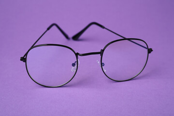 Stylish pair of glasses with black frame on purple background, closeup
