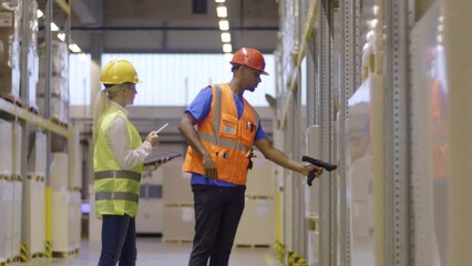 Storehouse coworkers scanning and using inventory app on digital tablet while standing in aisle near containers rack. Warehouse man and woman multicultural employees managing goods storaging
