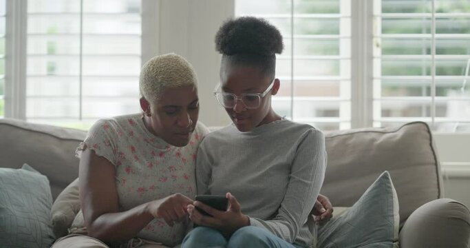 Mother and daughter looking at smart phone on sofa