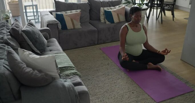 Pregnant woman sitting in lotus position on exercise mat in living room