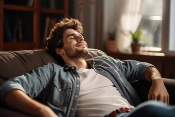 A young man is sitting on the sofa with his eyes closed and laughing