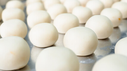 A lot of white round pastry dough is arranged in a stainless steel container. Shot from a side angle.