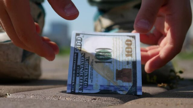 Close-up of a hundred dollar bill on the sidewalk and a boy passing by picks it up