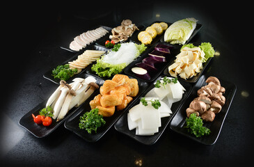 cold mixed raw vegetables,  beancurd, mushroom, carrot, noodle, tofu, lotus, corn in plate for steam boat hot pot ingredient on black marble table asian halal food cuisine menu for restaurant