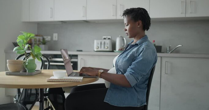 Pregnant woman working on laptop in kitchen