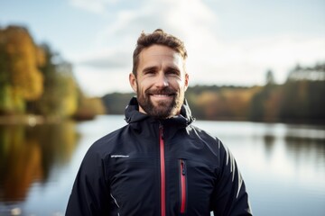 Portrait of a handsome young man in sportswear smiling at camera while standing by the lake.
