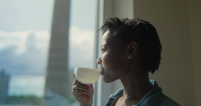 Woman drinking coffee while looking through window at home