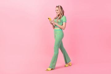 Full body photo of pretty young girl walking telephone read comment wear trendy green print outfit isolated on pink color background