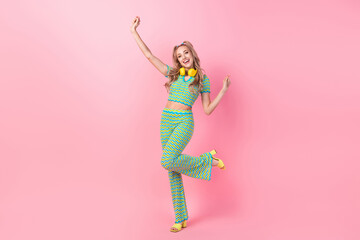 Full size photo of attractive young woman dancing raise hands headphones wear trendy green print clothes isolated on pink color background
