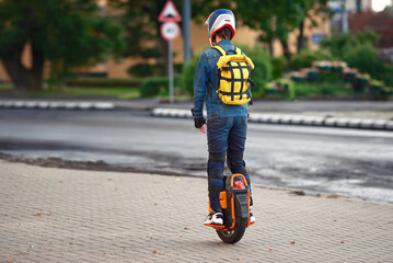 Boy with backpack in protective gear rides on electric unicycle. Man with knee pads, helmet and wrist protection on electric unicycle (EUC). Driving around city streets on electric monowheel. © Tricky Shark
