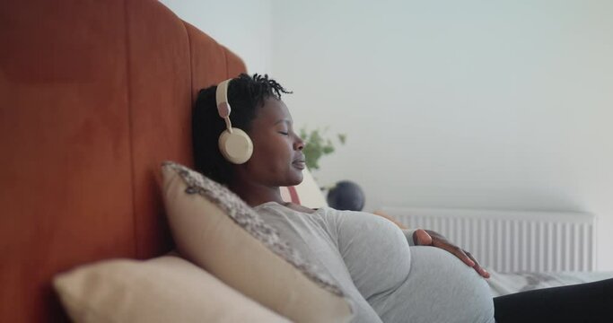 Pregnant woman listening to music while resting on bed
