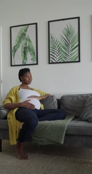 Pregnant woman touching belly while resting on sofa in living room