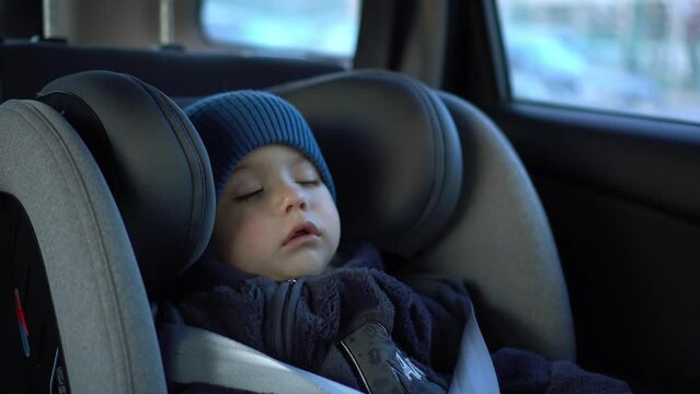 A small child sleeps in a car seat in a parking