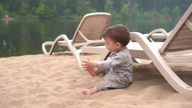 The child plays sits on the sand. A little boy