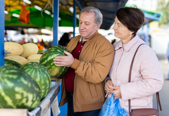 Elderly man and a woman buy a watermelon at an market
