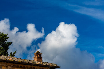Tuscany, Italy, tiled roof with one chimney, blue sky background with beautiful puffy clouds