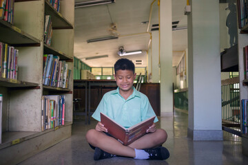 At the library, a young boy of Asian descent is deeply engrossed in reading a book during his break.