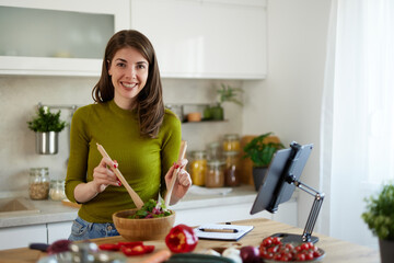 Young woman standing in the kitchen making a salad using online recipe