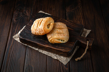 Bun from puff pastry with cottage cheese and greens on brown boards. For decoration of bakery sales outlets. Bakery products. Fresh bakery.