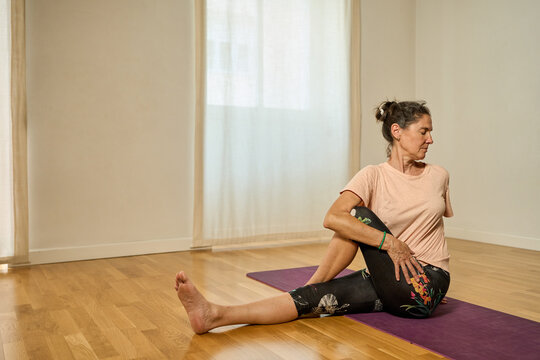 Mujer haciendo yoga en casa en postura de equilibrio sobre una pierna. Postura de ardha matsyendrasana o media torsi&oacute;n espinal.