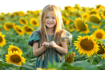 The cute little girl in a green dress with long beautiful hair laughing in a field of sunflowers. Portrait of a beautiful child enjoying nature at sunset. Little explorers.