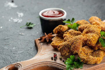 Homemade chicken nuggets with herbs and ketchup on a dark background, place for text, top view