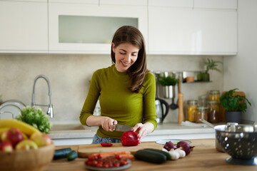 Woman chopping red bell pepper on the wooden board in the kitchen