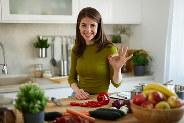 Woman chopping red bell pepper on the wooden board in the kitchen