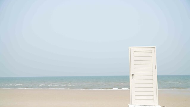 opened door with key in lock in beach,White wooden door at the beach with blue sky and sea background.