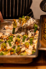 The cook puts salmon with mushrooms in a creamy sauce under the zucchini flowers on a plate