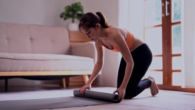 Beautiful young Asian athletic woman wearing sportswear  laying out yoga mat for exercise in a clearing floor at home, Concept of healthy lifestyle