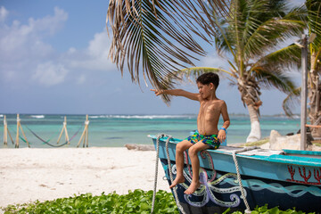 Beautiful little boy sitting on a boat pointing at something at the beach