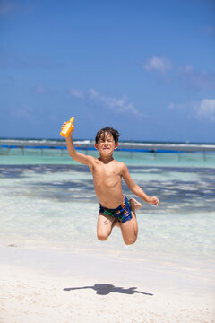 Beautiful little boy on a beach jumping with sunscreen