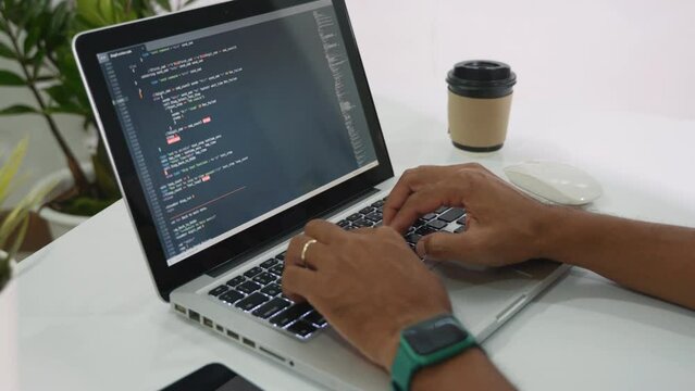 Web application development. programmer man writing program code sitting at workplace in office, software developer hands coding HTML programming with laptop computer, IT start up concept, back view