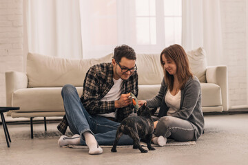 Happy couple is having fun and playing with their French Bulldog puppy at home.Family and animal...