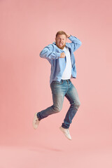 Full-length image of bearded mature man in casual clothes emotionally jumping and shouting over pink studio background. Concept of human emotions, lifestyle, facial expression, ad. Copy space for ad