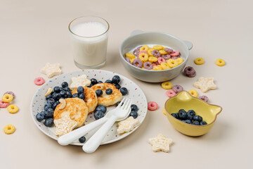 Children's breakfast. Cute children's plate with pancakes and  blueberries and  bowl with colorful cereal rings in milk. Creative serving for baby.  Concept of kids menu, nutrition and feeding.