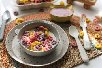 Colorful cereal rings with milk in bowl. Dry children's breakfast. Cute children's plates and bowls with tasty food. Creative serving for baby. Concept of kids menu, nutrition and feeding.