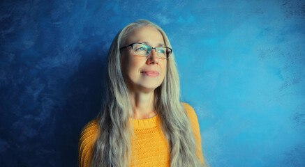 Portrait of happy smiling middle-aged woman in eyeglasses looking away. Senior blonde woman in casual on blue background