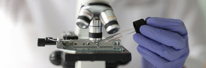 Scientist working with pipette and microscope in laboratory.