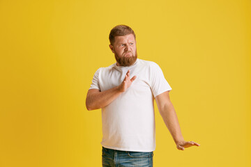 Bearded man in white t-shirt showing gesture of rejection against yellow studio background. Saying no. Concept of human emotions, lifestyle, facial expression, ad. Copy space for ad
