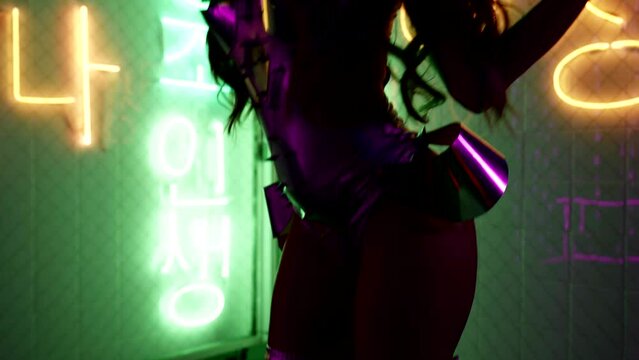 dark silhouette of sexy lady in bdsm suit and high heels shoes against neon lights in nightclub