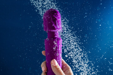 A woman washes a purple vibrator under the shower. Waterproof sex toy on a blue background.