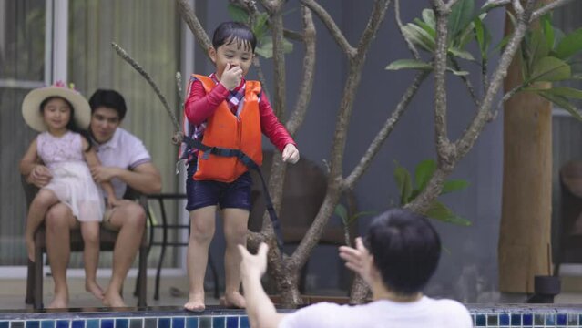 Asian family swimming in the pool on a happy vacation. A father teaches swimming to his child wearing a life jacket. Summer vacation activities